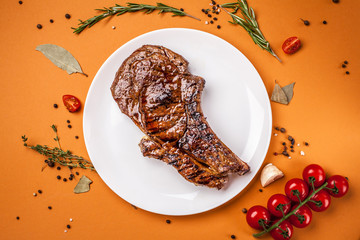 A large and juicy piece of roast lamb steak, veal, pork or beef lies on a white ceramic plate with spices, next to the fork and knife. Top view, copy space