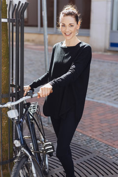 lächelnde, elegante frau mit ihrem fahrrad in der stadt