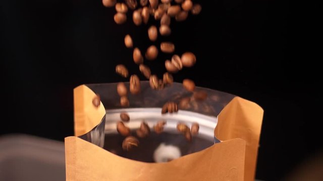 Just roasted coffee beans are poured down to the packaging in roasting cafe workshop slow motion