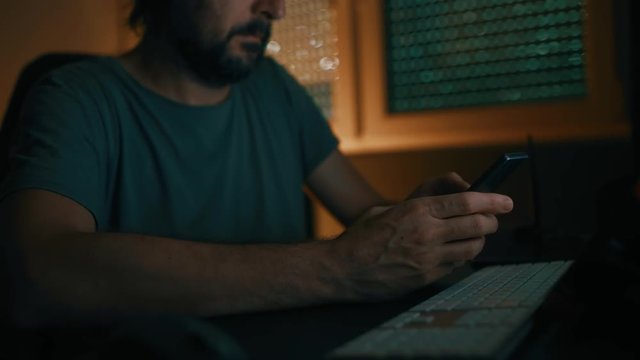 Freelancer using smartphone in home office late at night, low key footage