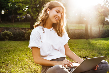 Portrait of attractive young woman sitting on green grass in park with legs crossed during summer...