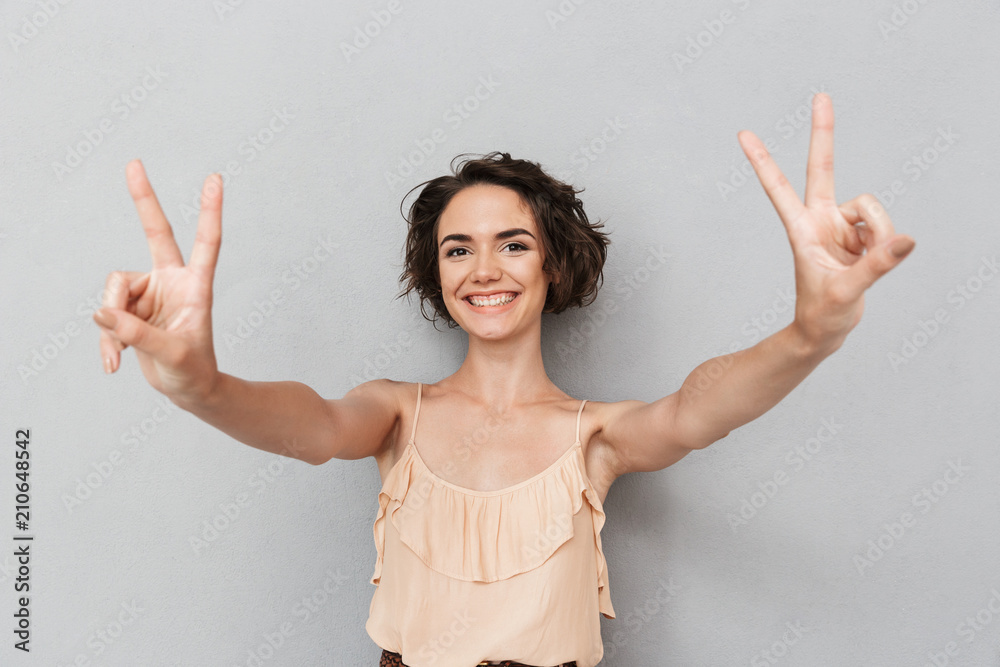 Sticker Portrait of a cheerful young woman showing peace gesture