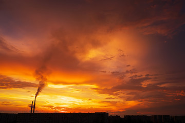 Colorful Magic Sunset. Roofs of city houses during sunrise. Birds flying in the sky. Dark smoke coming from the thermal power plant pipe.
