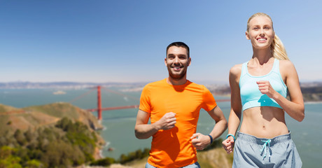 fitness, sport and healthy lifestyle concept - smiling couple running over golden gate bridge in san francisco bay background