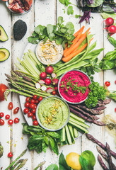 Healthy raw summer vegan snack plate. Flat-lay of chickpea, beetroot, spinach hummus dips with colorful vegetables and greens on white background, top view. Clean eating, dieting, vegan party food