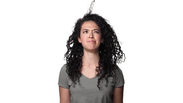 Portrait of brunette woman 20s with messy curly hair having fun and blowing off curl from her face, isolated over white background slow motion. Concept of emotions