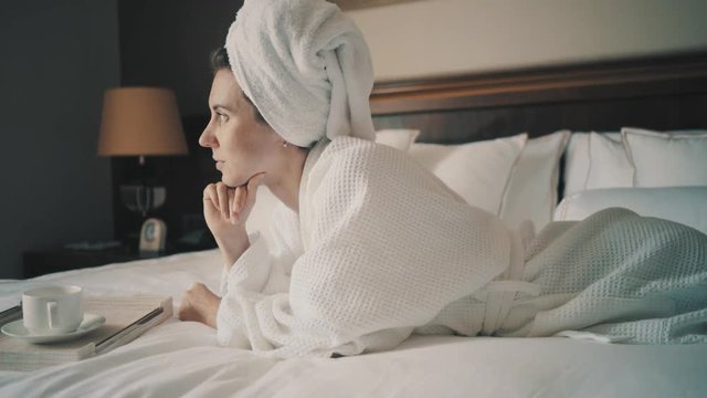 Woman drinks coffee on sunny morning in the room on the bed