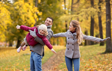 family, season and people concept - happy mother, father and little daughter playing at autumn park