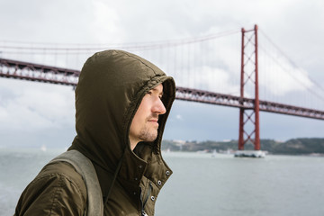 A young traveler or a tourist with a backpack on the waterfront in Lisbon in Portugal next to the 25th of April Bridge
