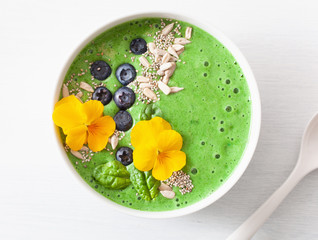 green spinach smoothie bowl with blueberry, chia seed and edible pansy flowers
