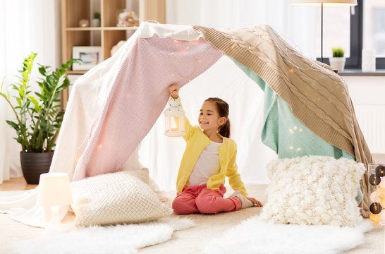 childhood and hygge concept - happy little girl with christmas lantern in kids tent at home