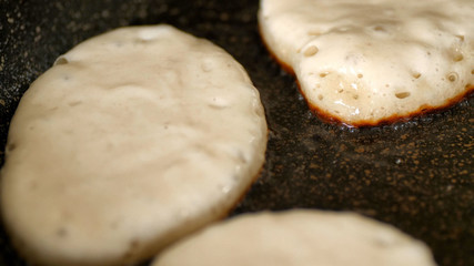 Fototapeta na wymiar Closeup view fresh white pancake dough mixture frying in bubble vegetable oil on preheat cast iron pan at home