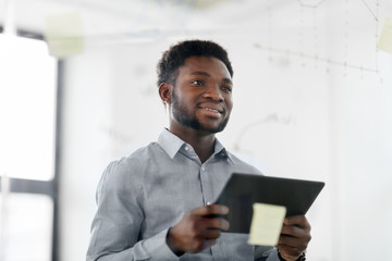 Fototapeta premium business and people concept - african american businessman with tablet pc computer working on at charts on office glass board