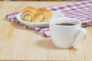 Two croissants on a white saucer next to a cup of coffee