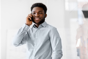 business, technology, communication and people concept - african american businessman calling on smartphone at office glass board