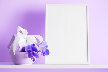 Photo frame mock up, beautiful flowers bouquet on the shelf, gift with white satin bow, lilac orchid on violet wall background. 