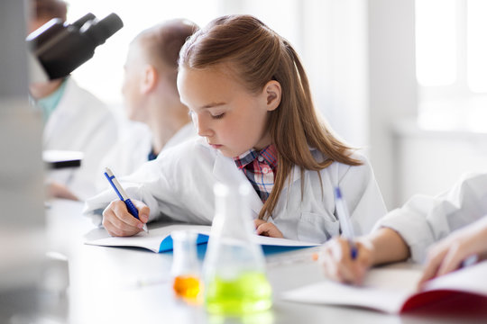 education, science and children concept - kids studying chemistry at school laboratory and writing to workbooks
