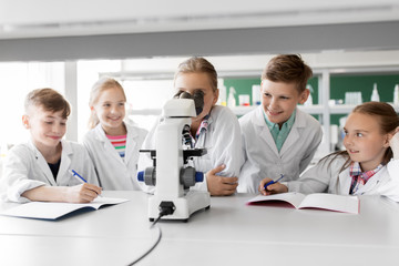 education, science and children concept - kids or students with microscope studying biology at school laboratory