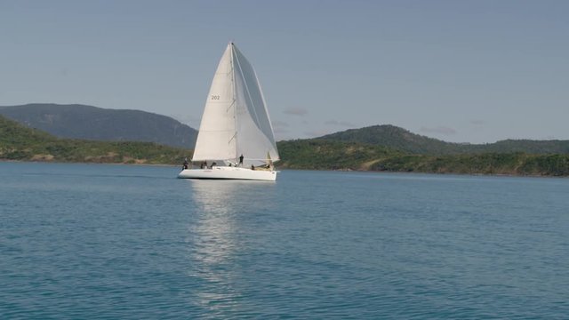 A moving shot of a sailboat with people aboard. The sailboat has a huge mast.