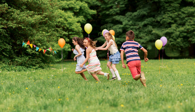 friendship, childhood, leisure and people concept - group of happy kids or friends playing tag game at birthday party in summer park