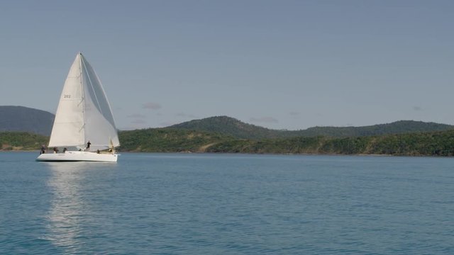 A moving shot in the ocean. The shot showed a white beautiful sailboat boarded with people.