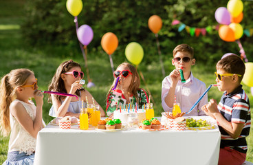 holidays, childhood and celebration concept - happy kids with cake blowing party horns and having...