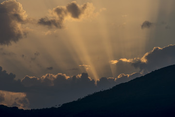 Rays of light filter through the clouds in a beautiful sunset behind the mountain