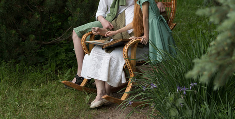 memories of the elderly. grandmother with her grandchildren sitting in a rocking chair in the garden and watching an old album with photos, recounts and remembers the family's story.