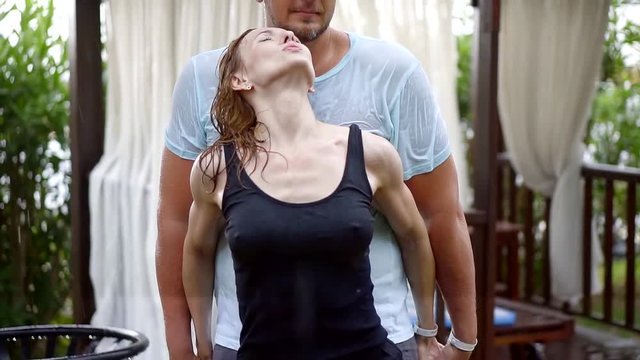 wet lovers are under rain in garden, redhead woman is snuggling to body of her boyfriend, holding hands