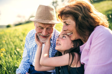 Senior couple with granddaughter outside in spring nature, relaxing on the grass.