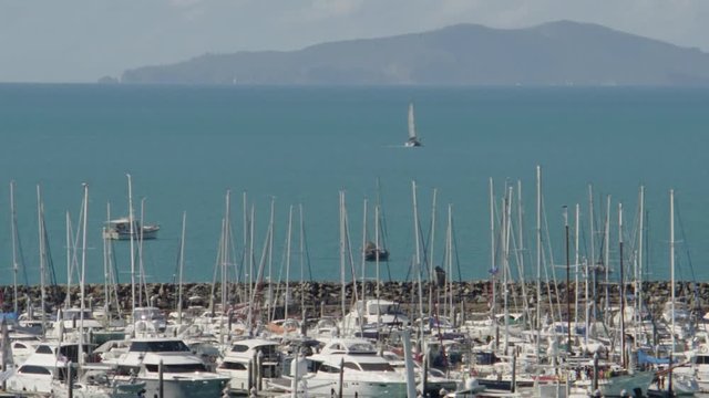 A tilt up shot of yachts that are docked in a pier. A sailboat is seen from afar.