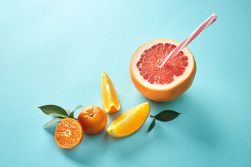 Orange and mandarin slice with halves grapefruit and red straw on blue background