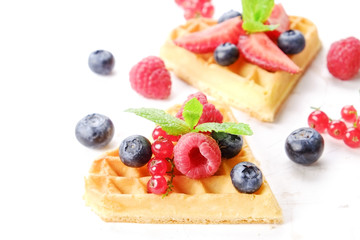 Heart shape belgium waffles with assorted berries mix, strawberry, blueberry, raspberry and red currant decorated with mint leaf on white ceramic plate. Close up, copy space, background, top view.