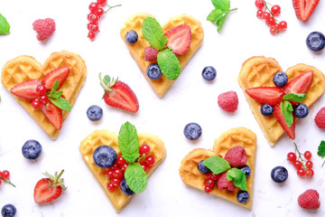 Heart shape belgium waffles with assorted berries mix, strawberry, blueberry, raspberry and red currant decorated with mint leaf on white ceramic plate. Close up, copy space, background, top view.