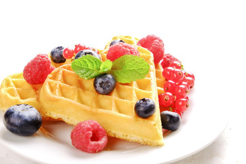 Heart shape belgium waffles with assorted berries mix, strawberry, blueberry, raspberry and red currant decorated with mint leaf on white ceramic plate. Close up, copy space, background, top view.