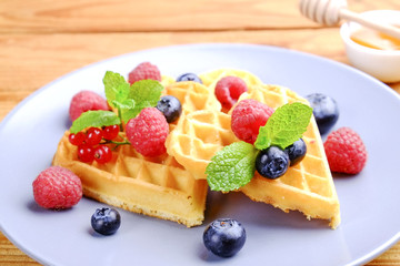 Heart shape belgium waffles with assorted berries mix, strawberry, blueberry, raspberry and red currant decorated with mint leaf on white ceramic plate. Close up, copy space, background, top view.