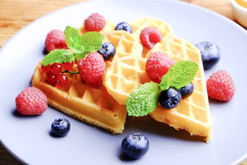 Heart shape belgium waffles with assorted berries mix, strawberry, blueberry, raspberry and red currant decorated with mint leaf on white ceramic plate. Close up, copy space, background, top view.