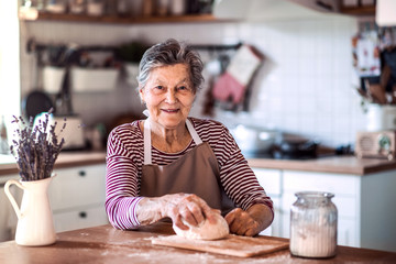 A senior woman kneading dough in the kitchen at home.