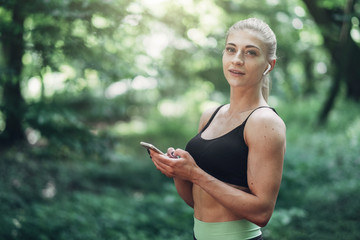 Woman Runner in the Summer Morning Park Listening to Music on Smartphone Using Bluetooth Earphones....