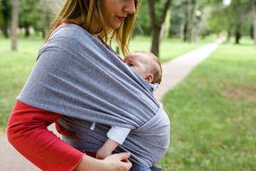 Mother holding baby in scarf baby carries outdoor