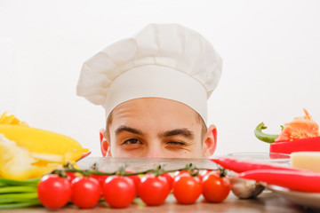 Man with cook cap on white background. Chef with vegetables on table. Cook with cheerful face in face close up.