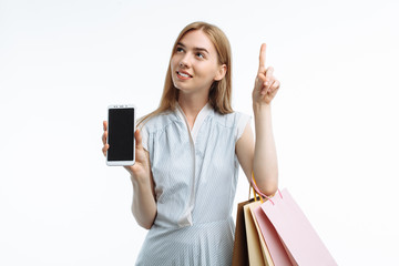 Young stylish girl, with gift bags, shopping, posing and showing smartphone with white screen, white background, for advertising, text insertion