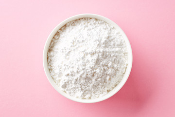 Bowl of powder sugar on white background, from above