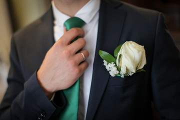 close up bridegroom in suit with buttonhole straightens his green tie