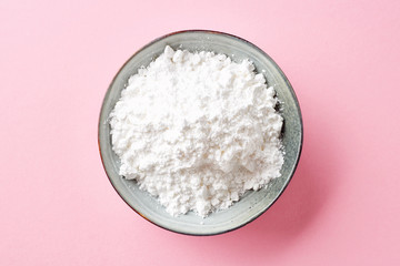 Bowl of powder sugar on white background, from above