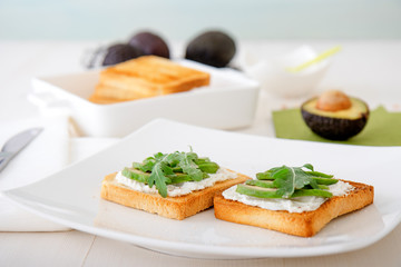 Roasted toasts with cream cheese and slices of avocado, leafs of rucola and pink Himalayan salt....