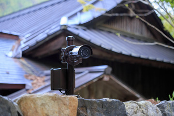 Surveillance camera on stone wall in front of traditional Japanese wooden building