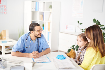 Portrait of smiling Middle-Eastern pediatrician talking to young mother and little girl during consultation in modern clinic, copy space