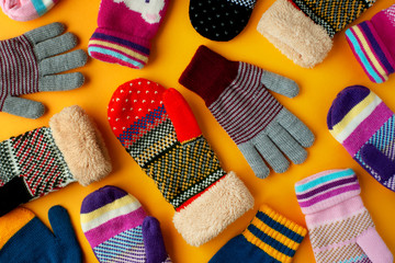 Warm clothes in the form of mittens and gloves. Colorful mittens and gloves scattered on a yellow background. View from above. - obrazy, fototapety, plakaty