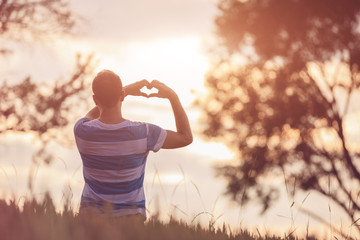 Man holding heart shape with hands in nature.